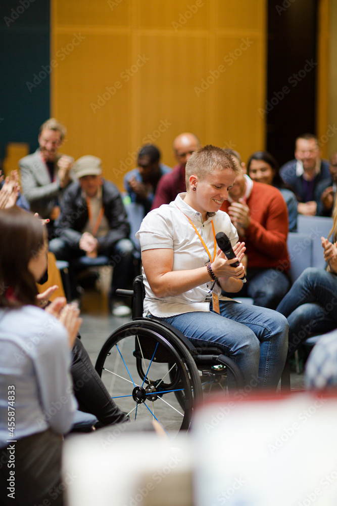 Audience watching male speaker in wheelchair talking on stage Audience watching male speaker in wheelchair talking on stage