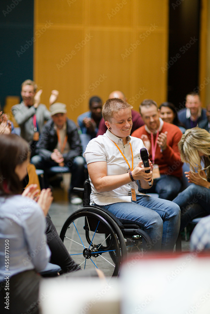 Audience watching male speaker in wheelchair talking on stage Audience watching male speaker in wheelchair talking on stage