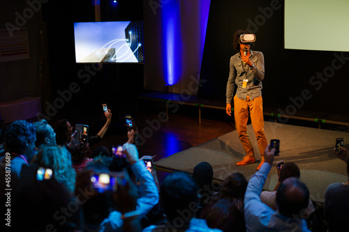 Audience watching male speaker with virtual reality simulator glasses on stage