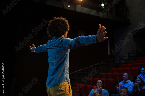 Audience watching male speaker with arms outstretched on stage