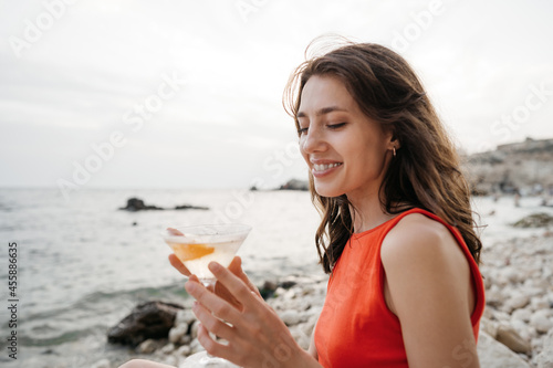Portrait of young woman with cocktail glass chilling on a beach