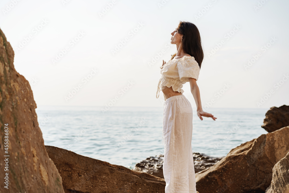 Young stylish woman standing on cliff at the sea at sunset Young stylish woman standing on cliff at the sea at sunset