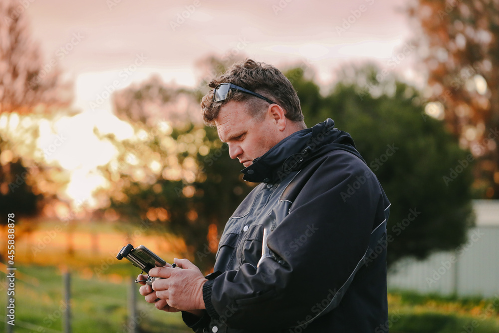Man flying drone holding remote control on country property at sunset Man flying drone holding remote control on country property at sunset