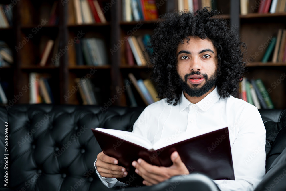 Serious handsome egyptian student preparing for lecture in library holding book Serious handsome egyptian student preparing for lecture in library holding book