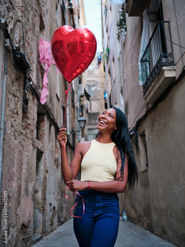 Young woman holding a heart balloon outdoors on the street.