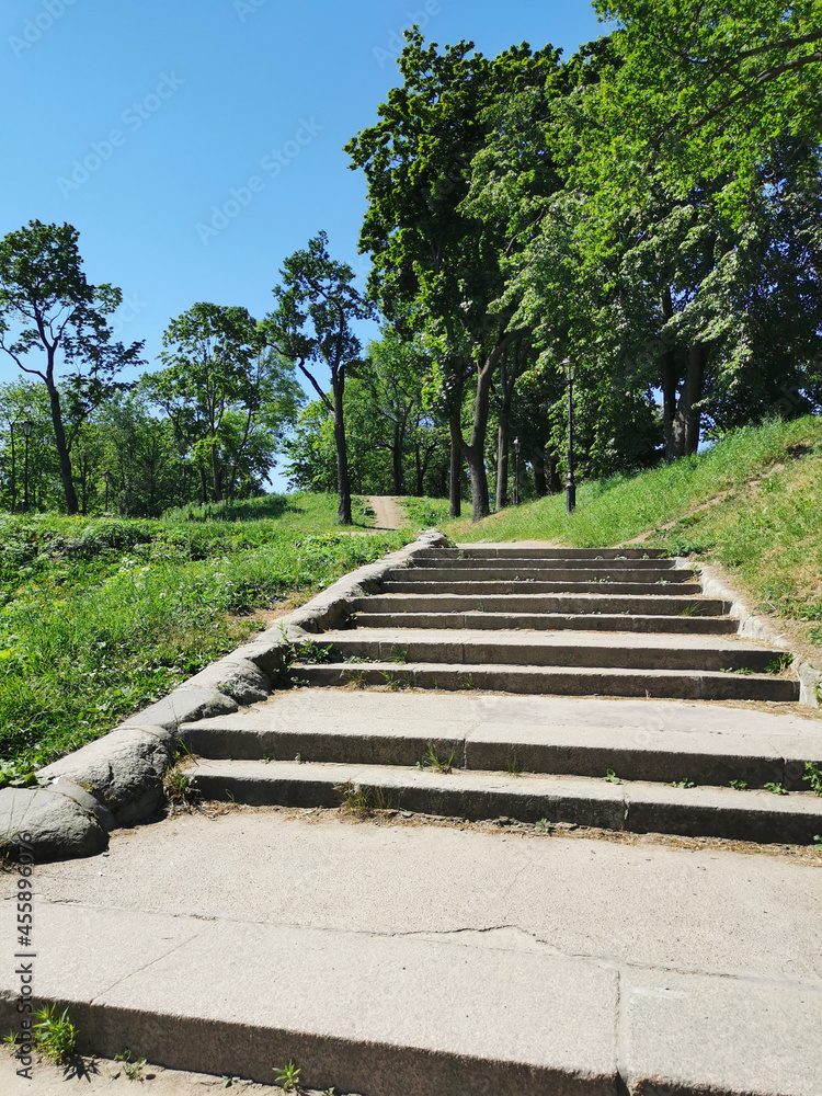 A view from below of a wide stone staircase in the Summer Garden of the city of Kronstadt against the background of a cloudless sky