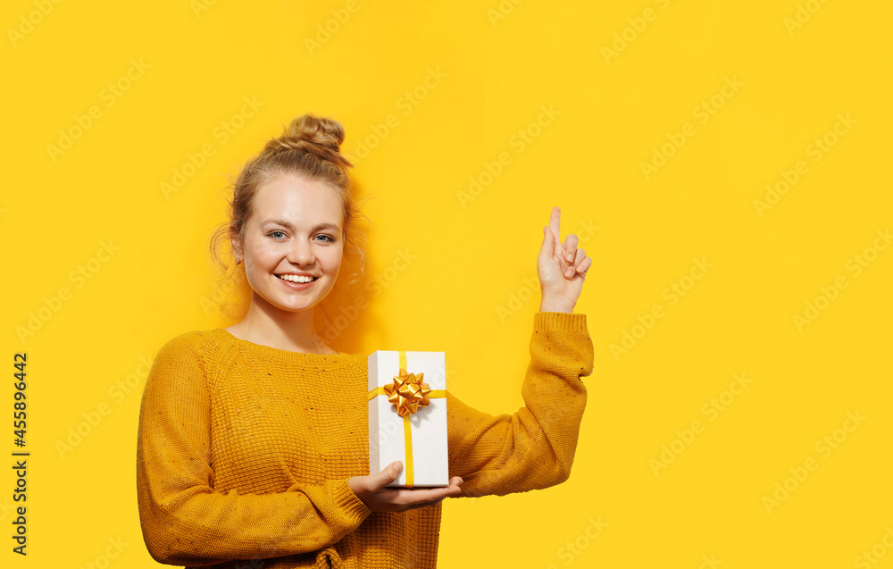 Smiling beautiful blonde young woman holding a gift box isolated over yellow background. Happy birthday, Christmas, Valentine's Day concept. Place for text. Smiling beautiful blonde young woman holding a gift box isolated over yellow background. Happy birthday, Christmas, Valentine's Day concept. Place for text.