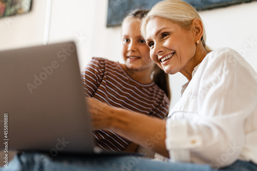 White mother and daughter smiling and using cellphone at home