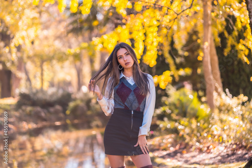 Autumn lifestyle, a young Caucasian brunette, in a black skirt and maroon boots in a fashionable pose, in a park by a lake