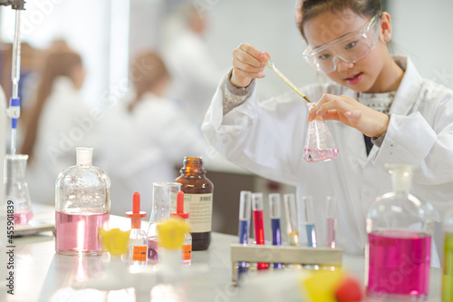 Girl student examining pink liquid, conducting scientific experiment in laboratory classroom