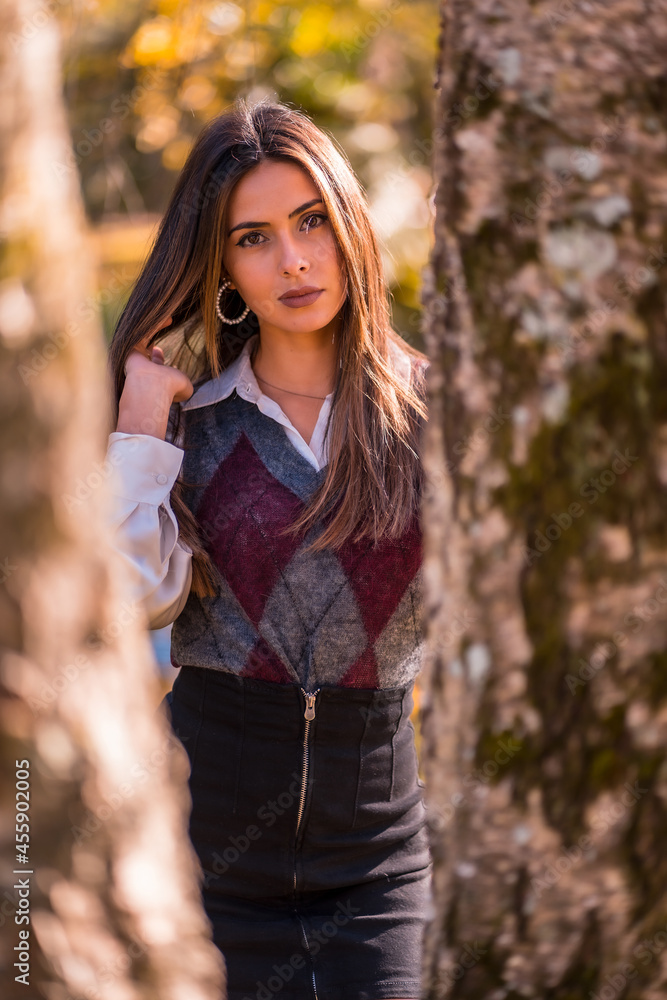 Autumn lifestyle, a young Caucasian brunette, in a park behind a tree with a smiling look Autumn lifestyle, a young Caucasian brunette, in a park behind a tree with a smiling look