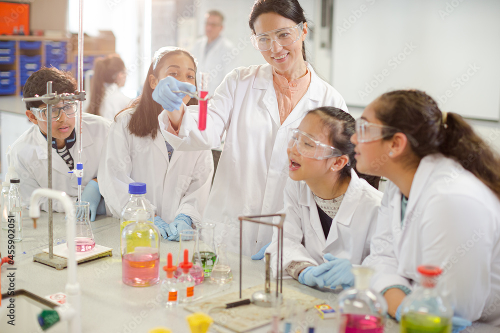 Female teacher and students conducting scientific experiment, watching liquid in test tube in laboratory classroom