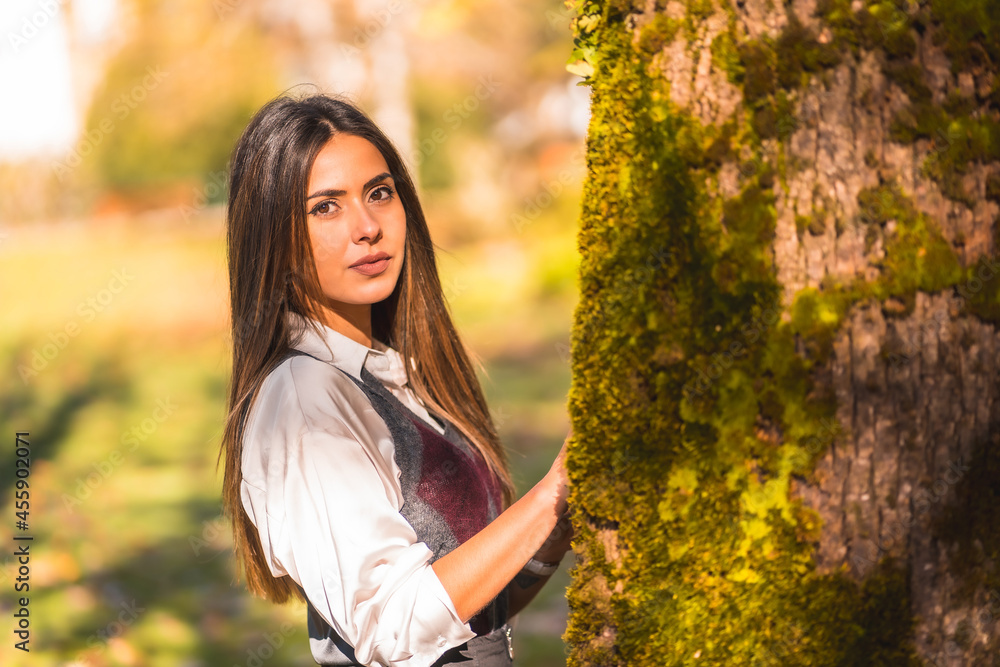 A young Caucasian brunette, in a park next to a tree one autumn afternoon A young Caucasian brunette, in a park next to a tree one autumn afternoon