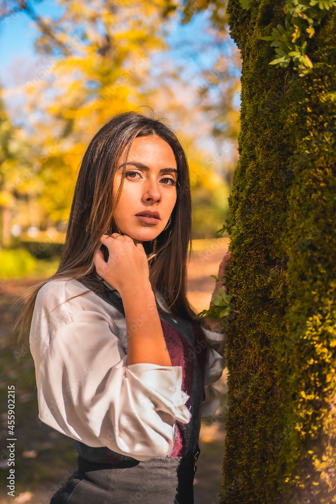 Lifestyle, a young brunette Caucasian college girl, in a park next to a tree one autumn afternoon in a fashionable pose Lifestyle, a young brunette Caucasian college girl, in a park next to a tree one autumn afternoon in a fashionable pose