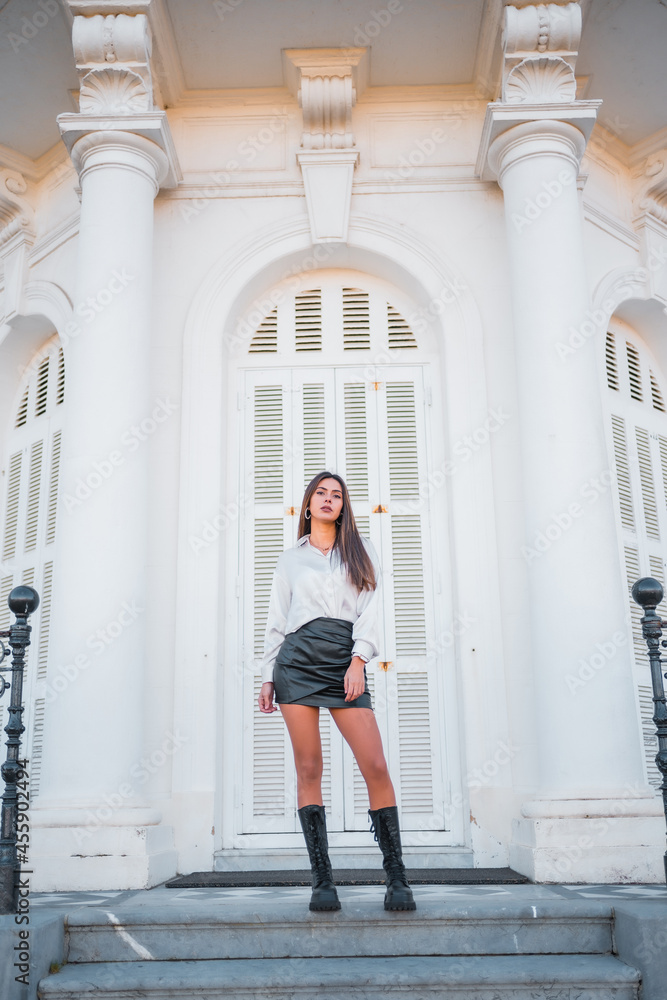 Lifestyle, a young brunette in a black leather skirt and shirt on the stairs of a white house