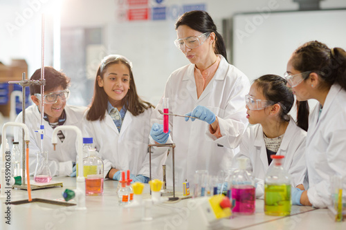 Female teacher and students conducting scientific experiment  watching liquid in test tube in laboratory classroom