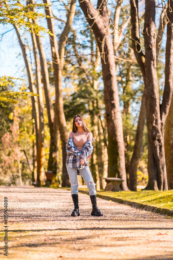 Autumn lifestyle, portrait of a young Caucasian brunette girl in a plaid wool sweater and ripped jeans in a park Autumn lifestyle, portrait of a young Caucasian brunette girl in a plaid wool sweater and ripped jeans in a park