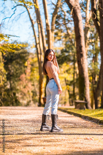 Fototapeta Naklejka Na Ścianę i Meble -  Lifestyle, young Caucasian brunette in a pink sweater and jeans walking in a park in autumn