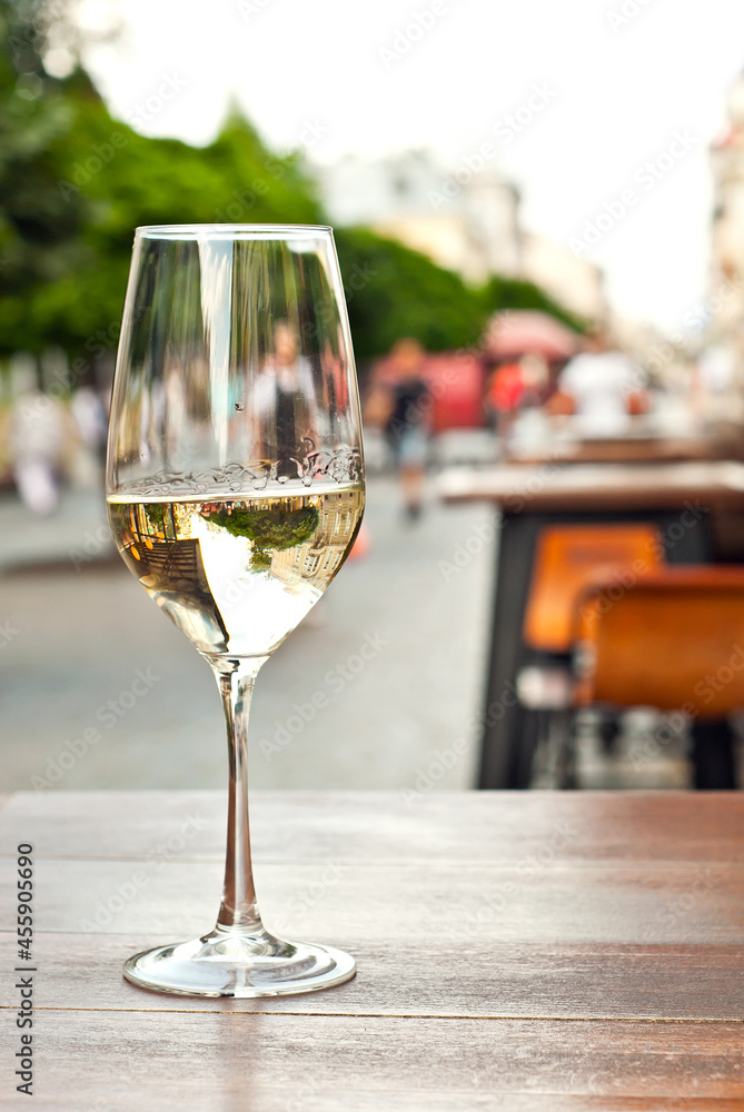 Obraz premium Glass of white wine close up. Alcoholic drink on a wooden table on a background of the city. Transparent wine on the summer terrace of the restaurant.