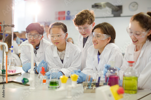 Curious students conducting scientific experiment, examining liquid in beaker in laboratory classroom © KOTO