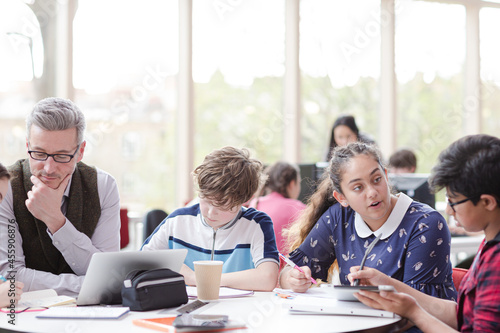 Male teacher and students using laptop at table