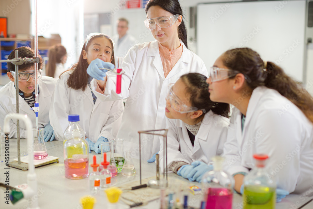 Female teacher and students conducting scientific experiment, watching liquid in test tube in laboratory classroom Female teacher and students conducting scientific experiment, watching liquid in test tube in laboratory classroom