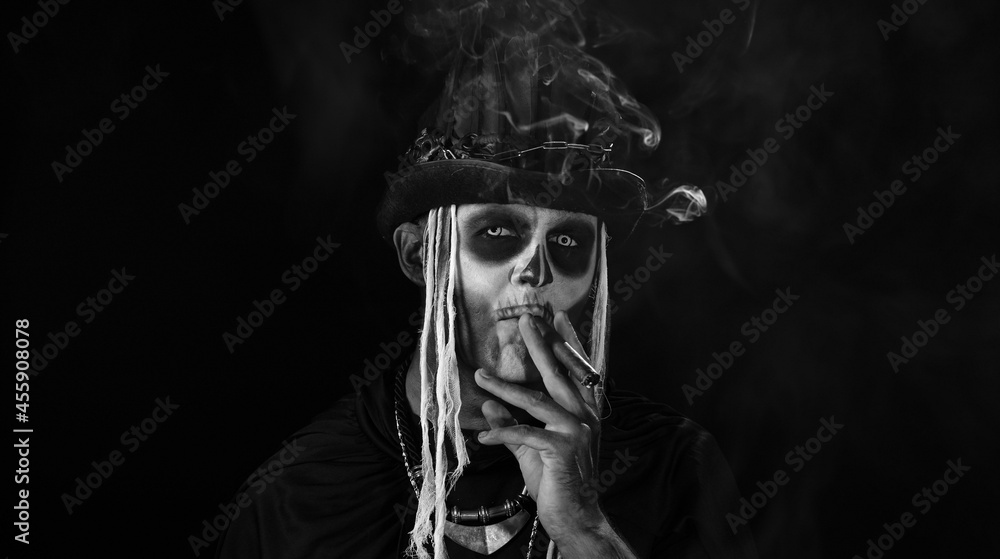 Sinister man with horrible Halloween skeleton makeup in costume with top-hat smoking cigar, making faces. Horror theme. Day of The Dead. Isolated on black background. Black and white portrait
