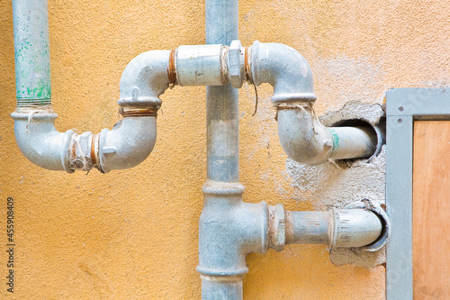 Galvanized steel metal pipes for water plumbing fixed to a brick and plaster wall with metal box for water meter