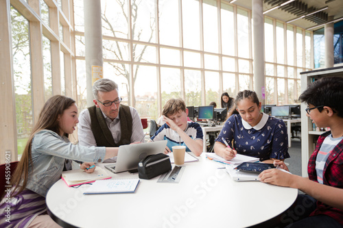 Male teacher and students using laptop at table