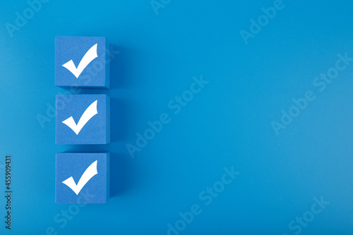 Modern minimal flat lay with three white checkmarks on blue cubes against blue background with copy space. Concept of questionary, checklist, to do list or planning 
