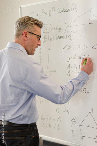 Male teacher writing at whiteboard in classroom