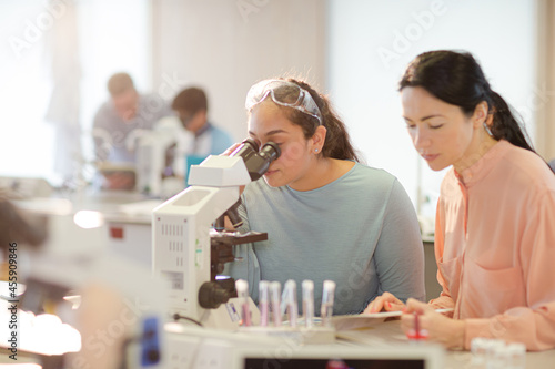 Female teacher and girl student conducting scientific experiment at microscope in laboratory classroom