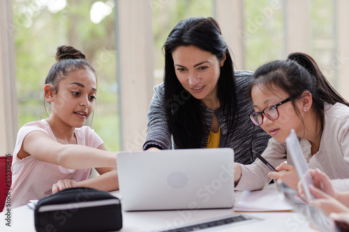 Female teacher and girl students using laptop at table