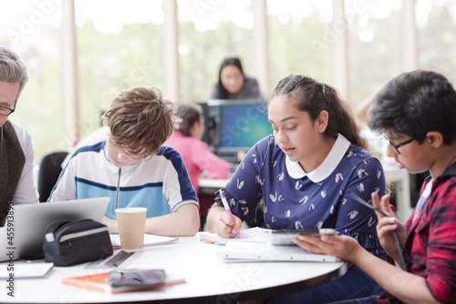 Male teacher and students using laptop at table