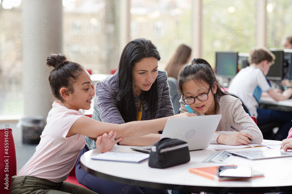 Female teacher and girl students using laptop at table Female teacher and girl students using laptop at table