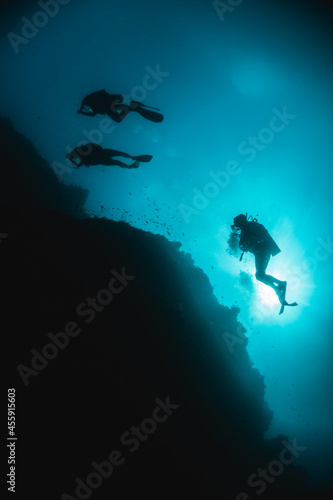 Scuba diver silhouettes swimming around coral reef in clear blue ocean