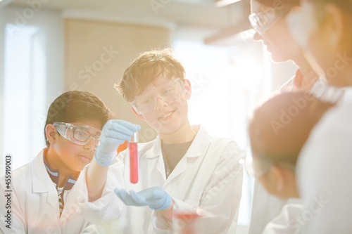 Female teacher and students examining liquid in test tube, conducting scientific experiment in laboratory classroom