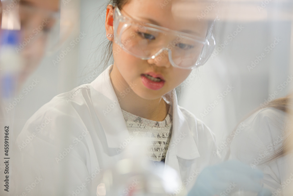 Girl student examining pink liquid, conducting scientific experiment in laboratory classroom Girl student examining pink liquid, conducting scientific experiment in laboratory classroom