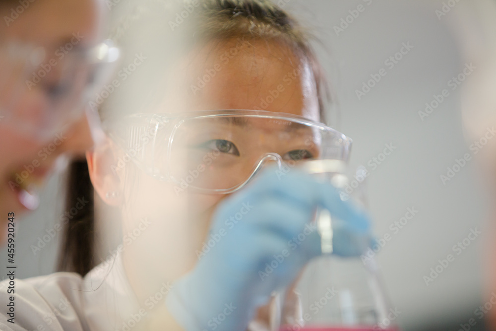 Girl student examining pink liquid, conducting scientific experiment in laboratory classroom Girl student examining pink liquid, conducting scientific experiment in laboratory classroom