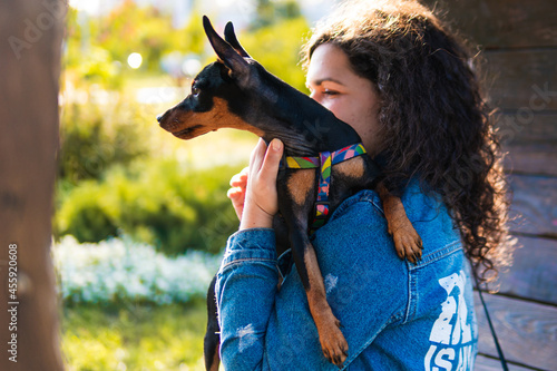 Young woman with her little dog outdoors. Black and Tan miniature pinscher female dog with owner in a park