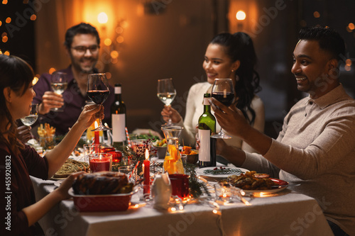 holidays  party and celebration concept - multiethnic group of happy friends having christmas dinner at home and drinking wine