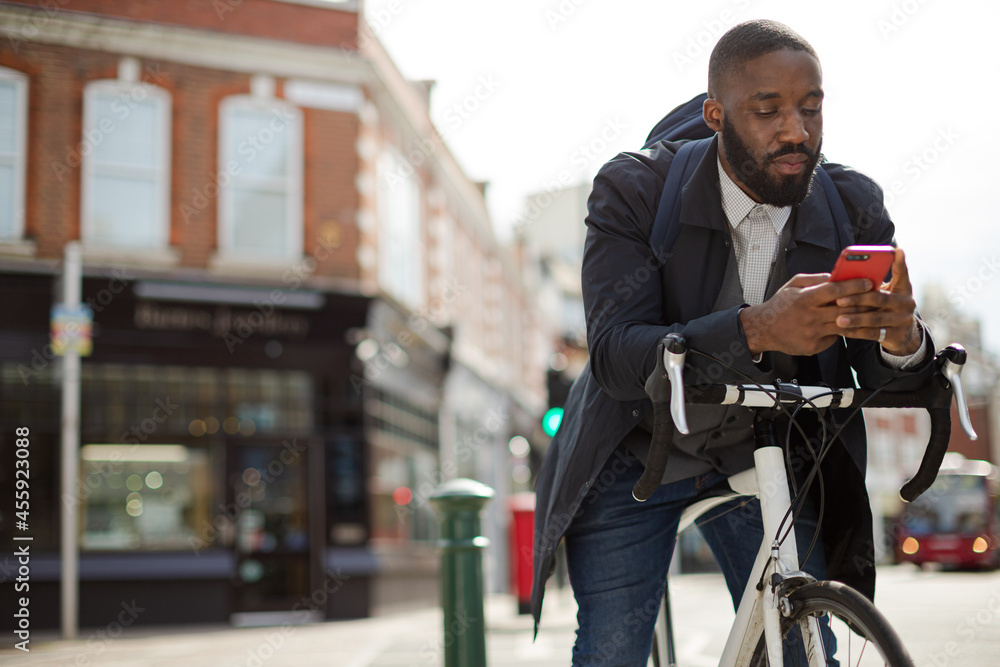 Young businessman commuting with bicycle, texting with cell phone on sunny urban street Young businessman commuting with bicycle, texting with cell phone on sunny urban street