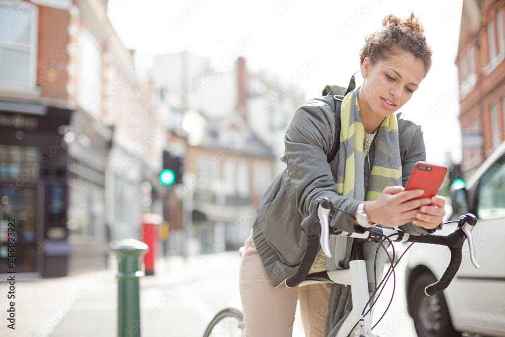 Young woman commuting on bicycle, texting with cell phone on sunny urban street Young woman commuting on bicycle, texting with cell phone on sunny urban street