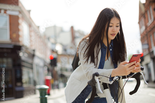 Young woman commuting on bicycle  texting with cell phone on sunny urban street