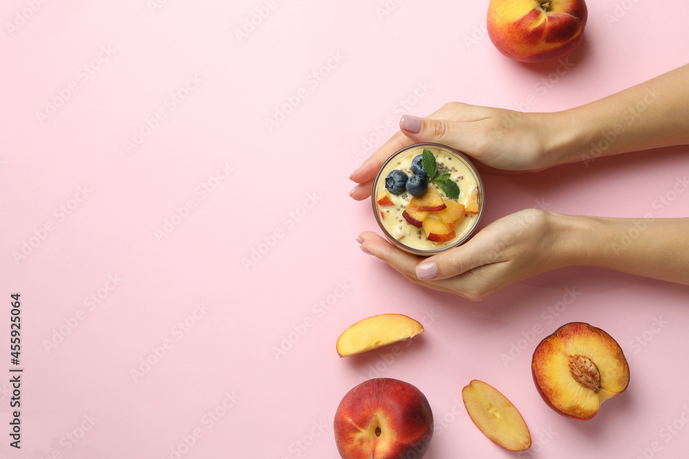 Female hands hold peach yogurt on pink background