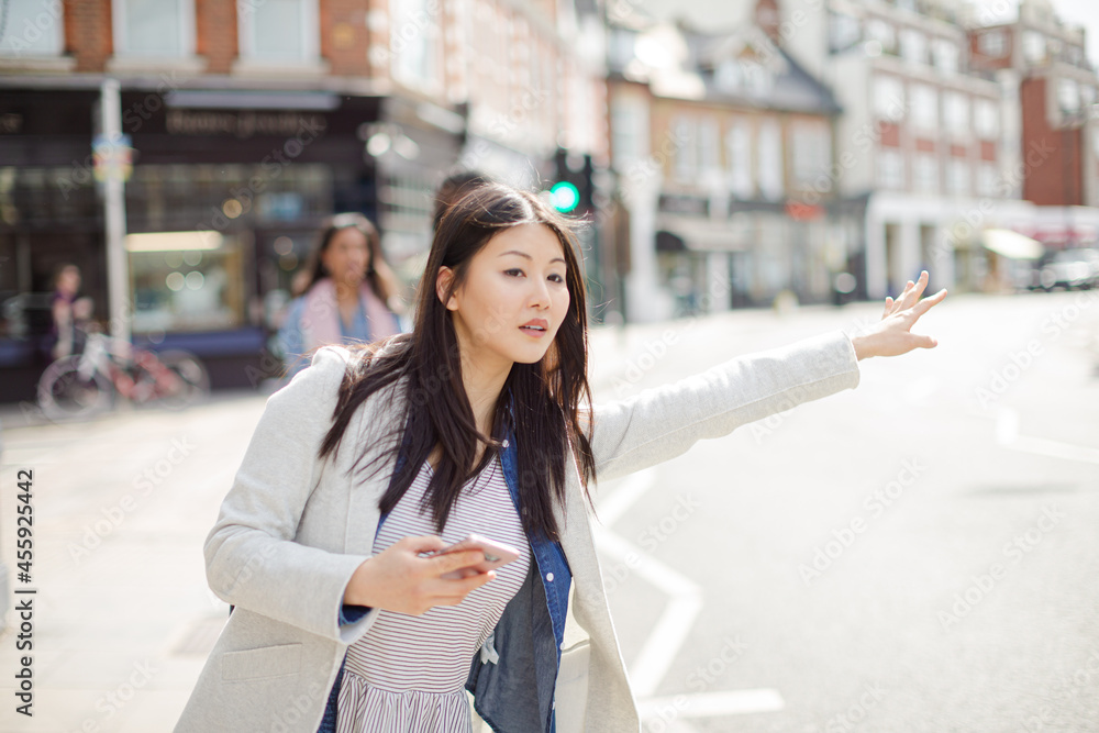 Young businesswoman with cell phone hailing taxi on sunny urban street Young businesswoman with cell phone hailing taxi on sunny urban street