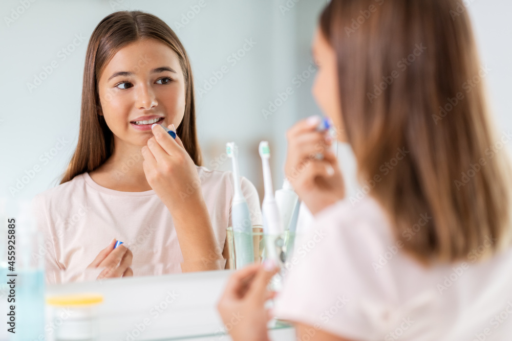 beauty and cosmetics concept - teenage girl applying lip balm and looking to mirror at home bathroom beauty and cosmetics concept - teenage girl applying lip balm and looking to mirror at home bathroom