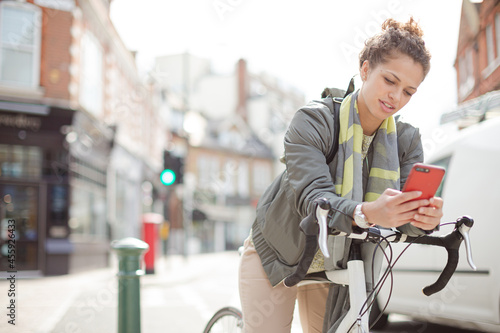 Young woman commuting on bicycle, texting with cell phone on sunny urban street © KOTO