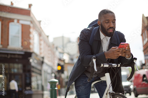 Young businessman commuting with bicycle, texting with cell phone on sunny urban street © KOTO