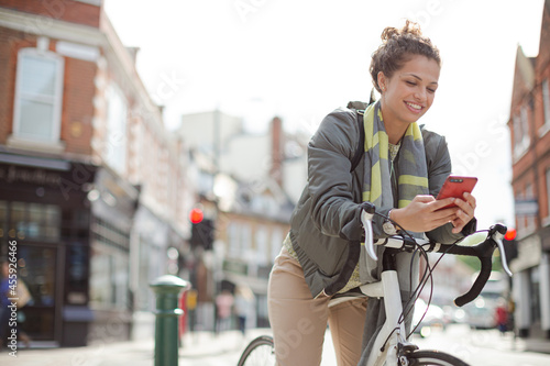 Young woman commuting on bicycle, texting with cell phone on sunny urban street © KOTO
